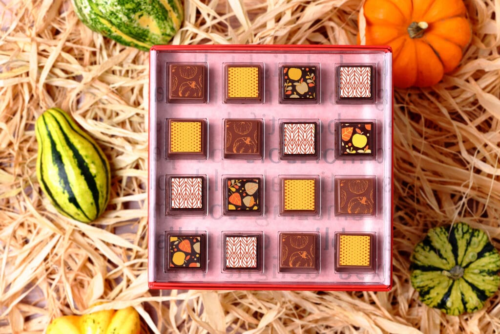 Delysia Chocolatier's 16-piece Modern Harvest Collection arranged in a box surrounded by pumpkins, gourds and straw.