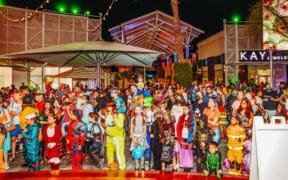 Large crowd of adults and children in Halloween costumes at Desert Ridge Marketplace during an evening celebration.