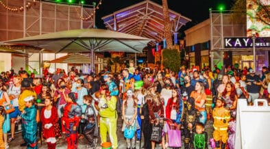Large crowd of adults and children in Halloween costumes at Desert Ridge Marketplace during an evening celebration.