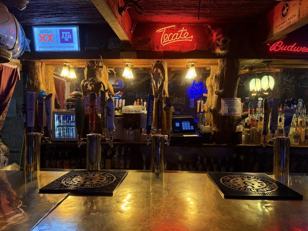 Rustic bar inside Dixie Chicken in College Station with neon signs, beer taps and Texas A&M memorabilia.