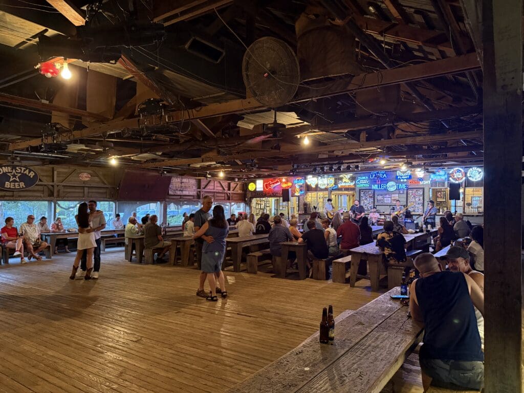 Couples dancing to a live band inside Gruene Hall, with wooden floors, long tables and neon signs.