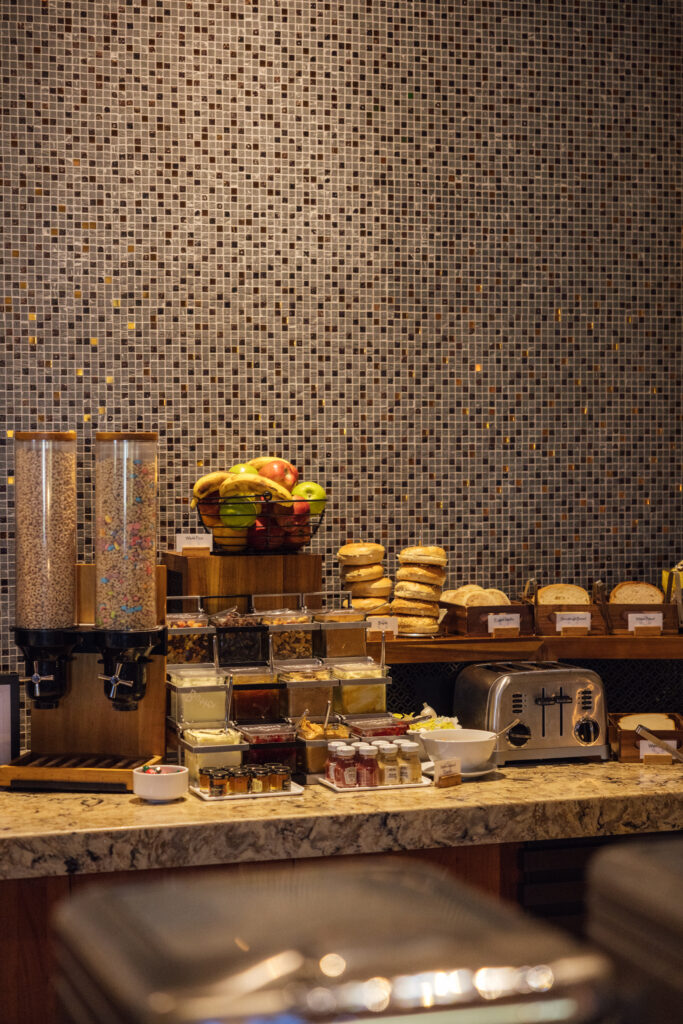 Breakfast buffet with cereal dispensers, fresh fruit, bagels, sliced bread and a toaster at Ko’sin.