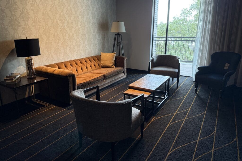 Sitting area at The George hotel with a tan tufted sofa, gray armchairs, wood coffee table and balcony doors.