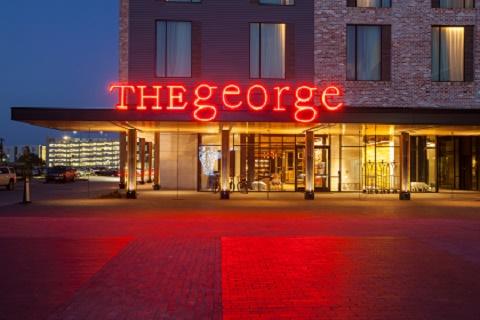 Exterior of The George hotel illuminated at night in College Station, Texas.